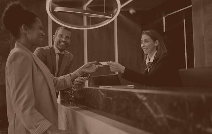 Photo of a hotel reception desk with receptionist handing over keycard to guest.